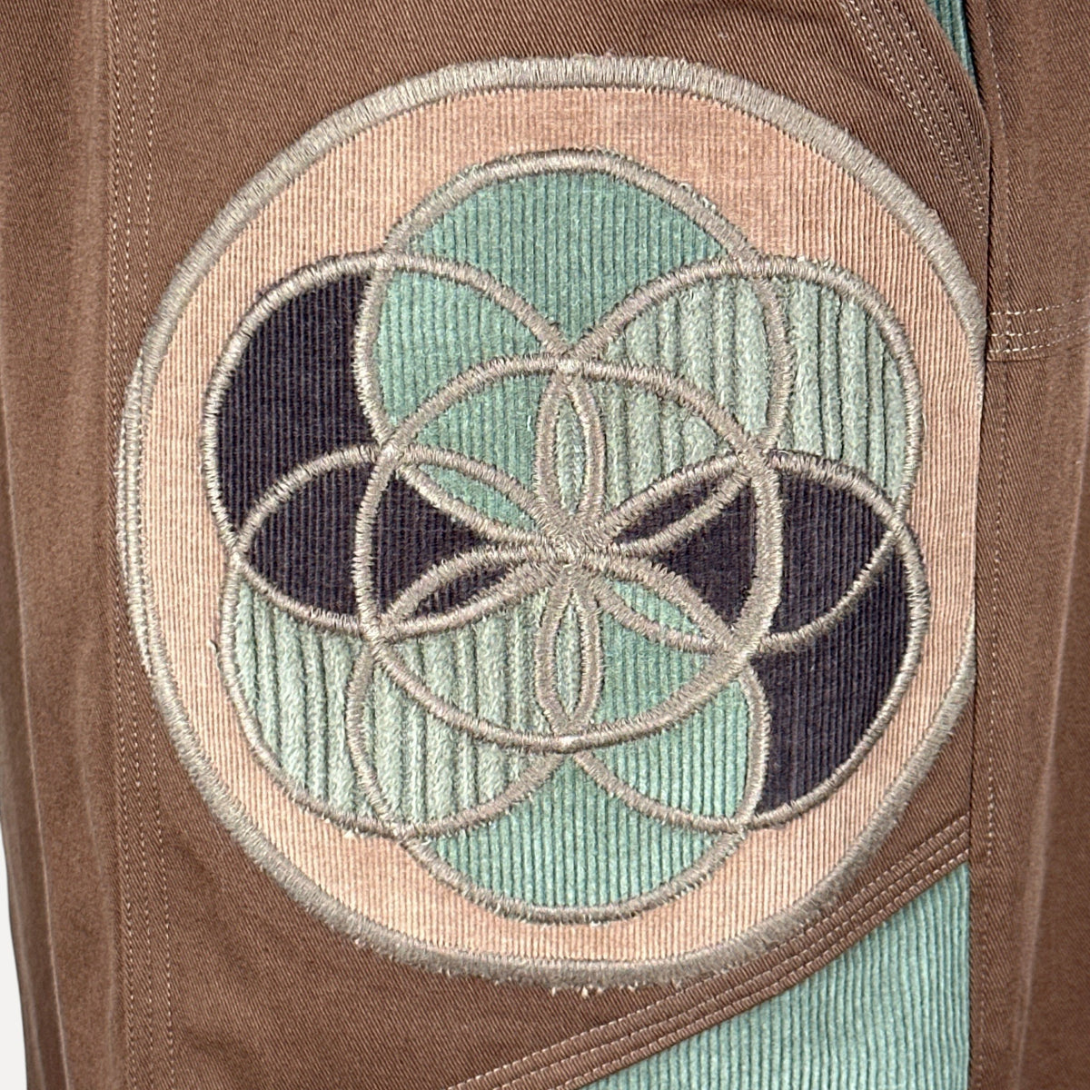 nowAwear brown twill shorts featuring a circular embroidered sacred geometry patch with teal and dark blue corduroy