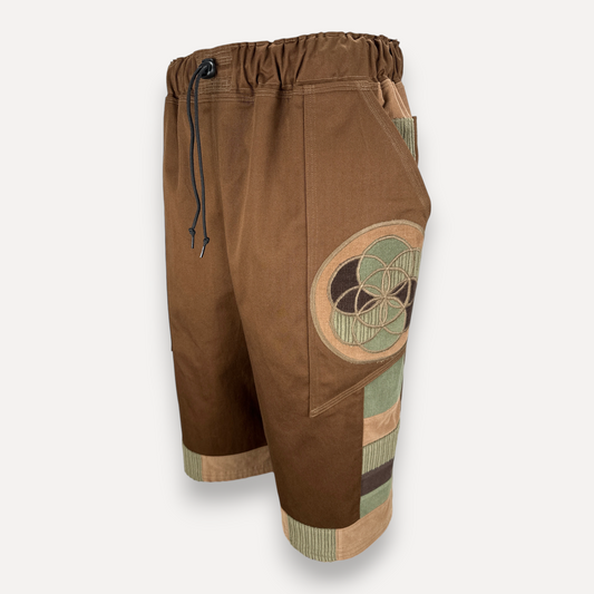nowAwear brown twill shorts featuring a circular geometric patch, elastic waistband, and green corduroy side panels.