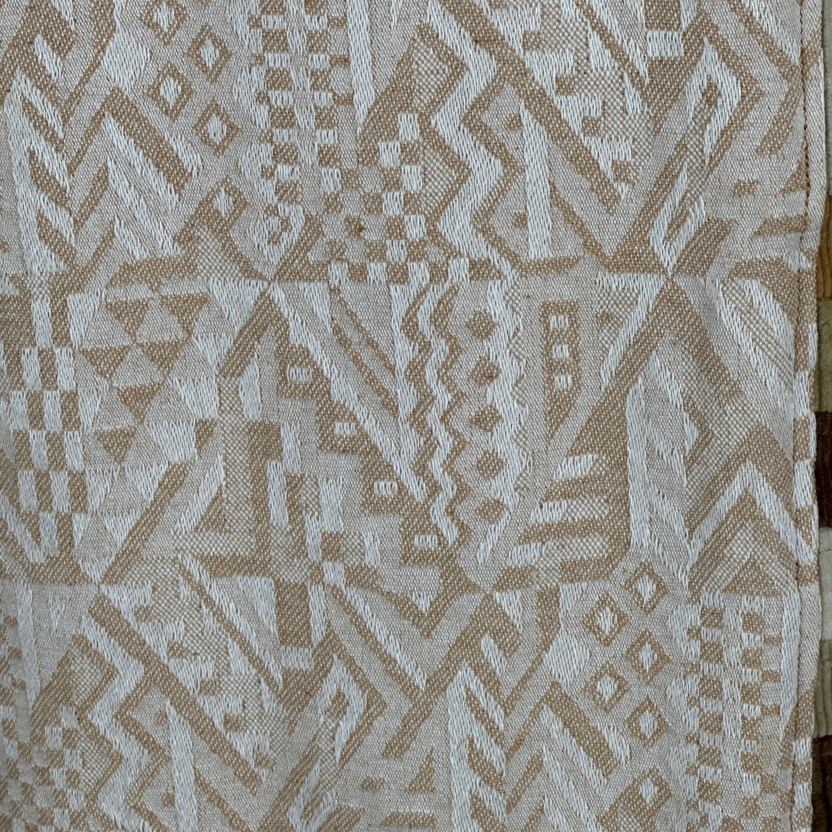 A close-up of woven fabric with an intricate geometric pattern in beige and off-white.