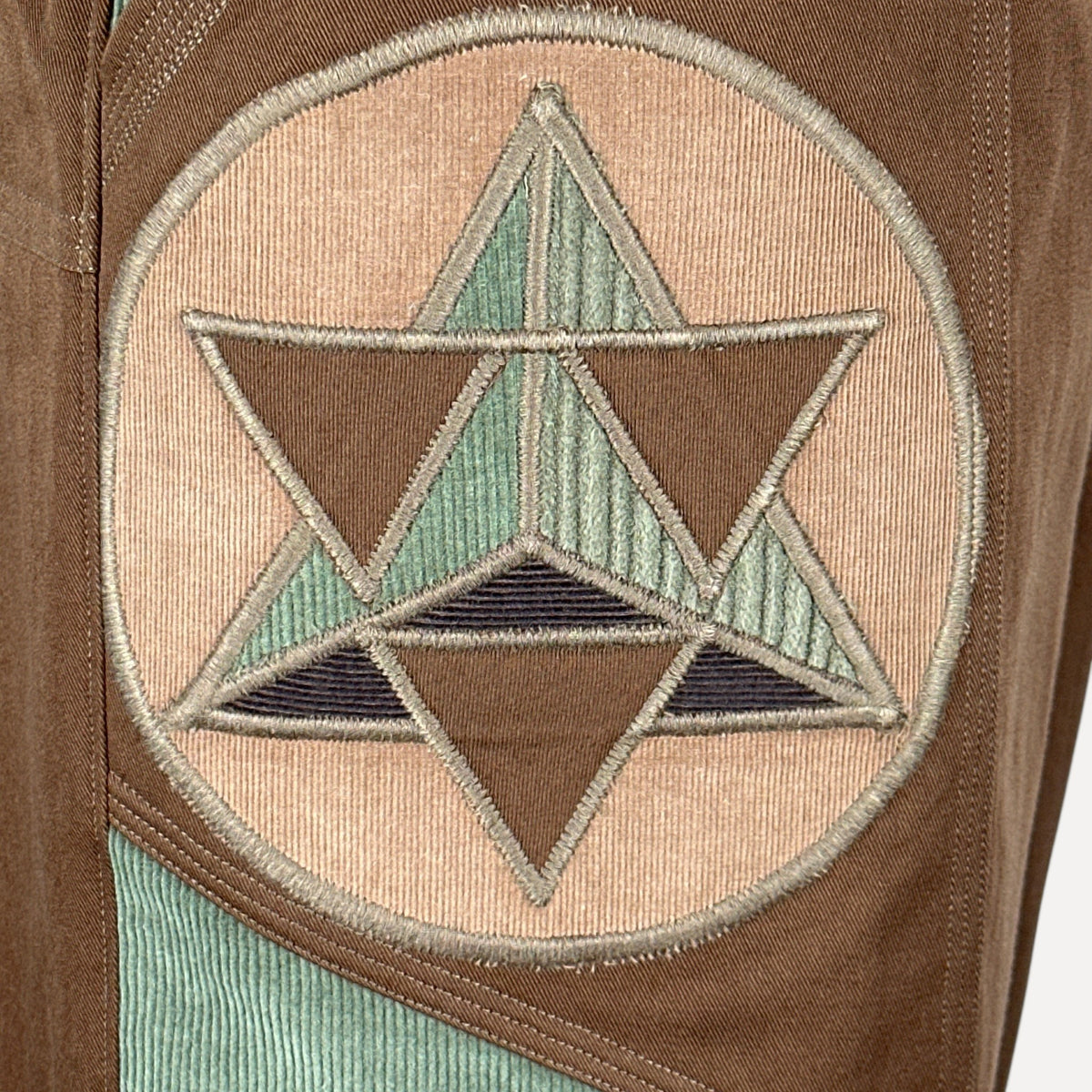 nowAwear brown twill shorts featuring a circular embroidered geometric star patch with green and dark accents