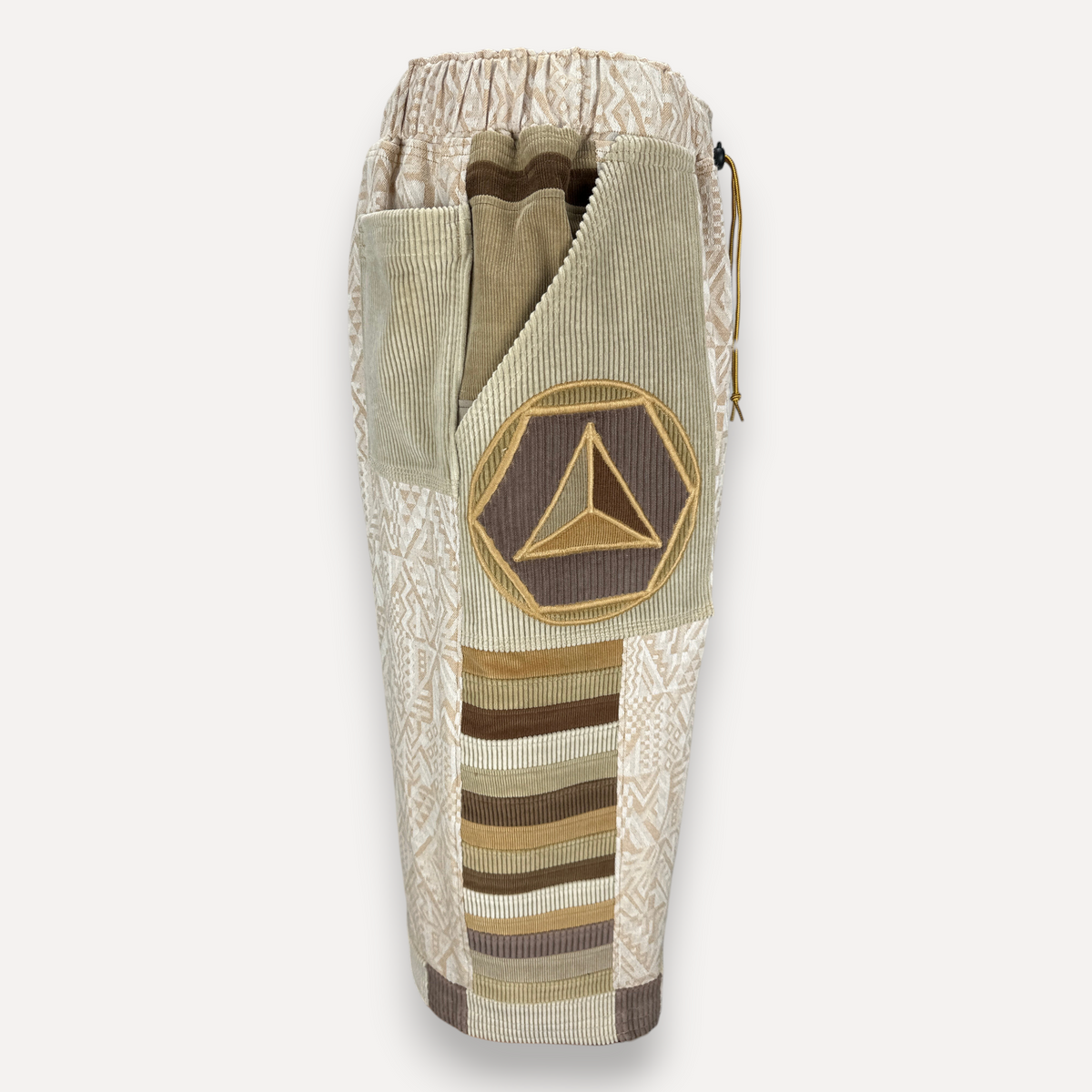 nowAwear shorts in beige and brown cotton with geometric patterns, corduroy panels, and a circular triangle patch.