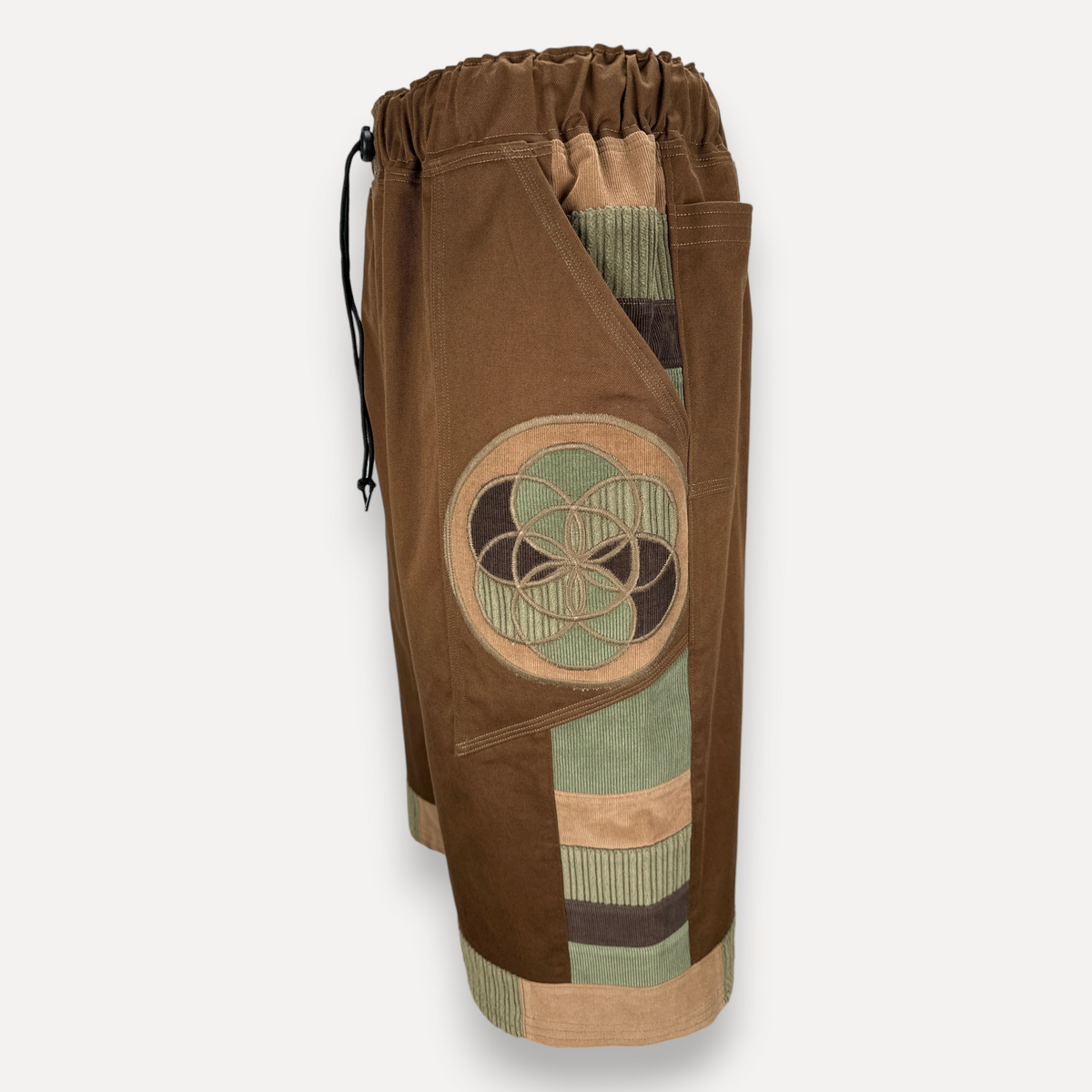 nowAwear brown twill shorts featuring a circular geometric patch, corduroy paneling, and an elastic drawstring waist.