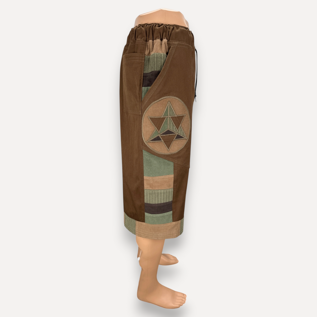 nowAwear brown twill shorts featuring a circular geometric patch, corduroy panels, and an elastic drawstring waist.