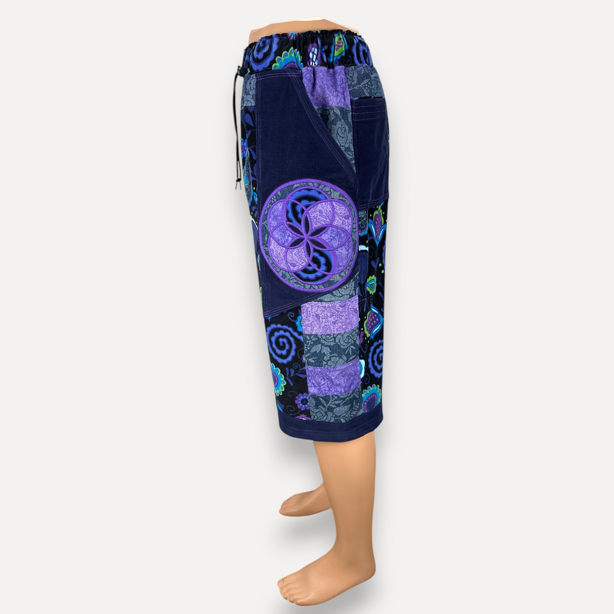 nowAwear knee-length shorts featuring a purple and blue patchwork design with floral patterns and a circular mandala print