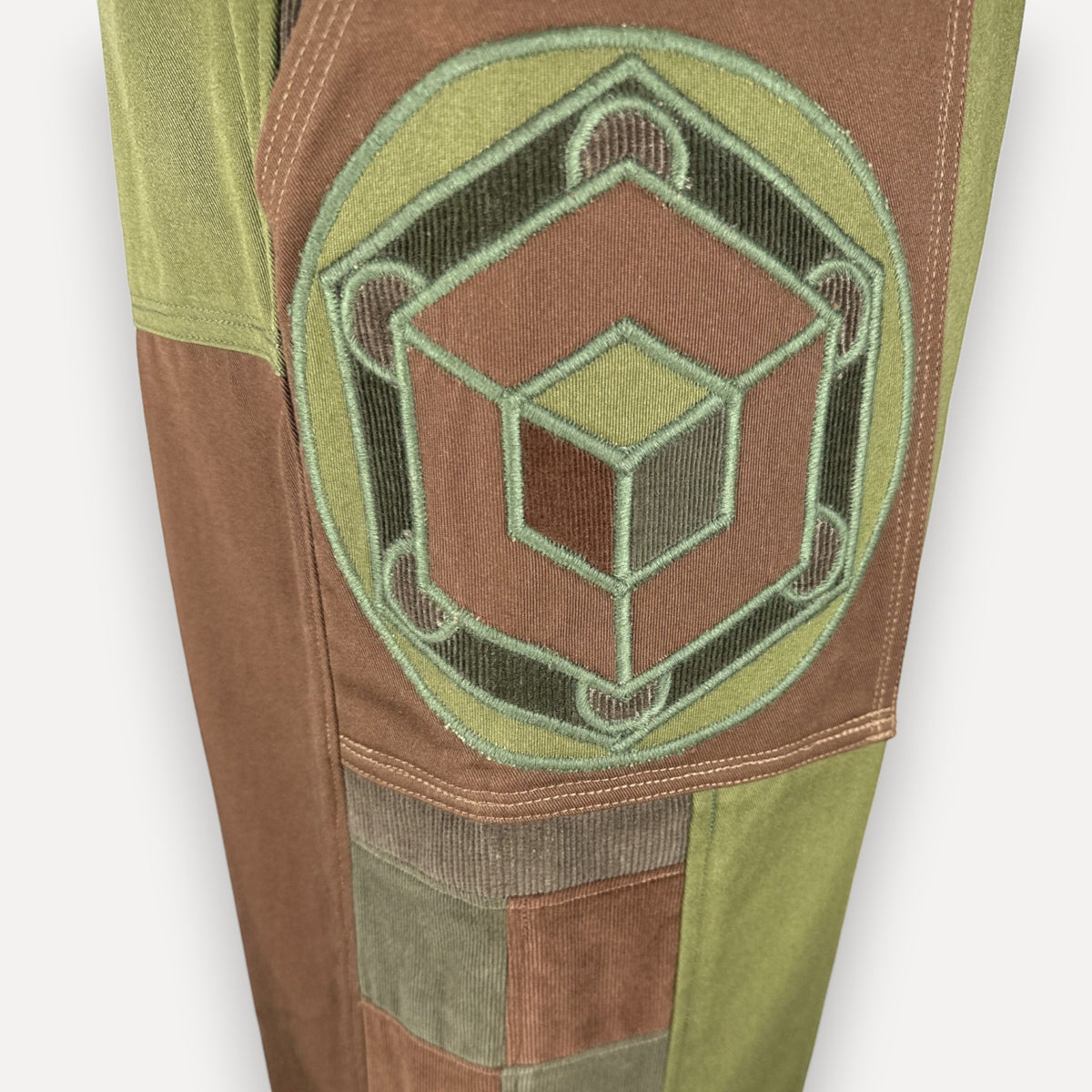 nowAwear shorts featuring a brown and green patchwork design with a large embroidered geometric cube emblem